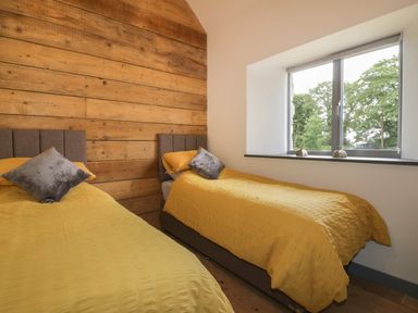 A bedroom with two single beds covered with yellow bedspreads and gray pillows next to a window and a wood paneled wall at The Corn Store in St Stephen