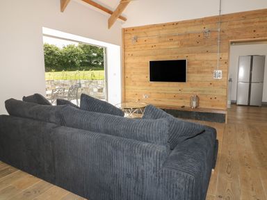 A living room with a black sofa a wall-mounted television wooden paneling and an open door to a kitchen with a silver refrigerator at The Corn Store in St Stephen