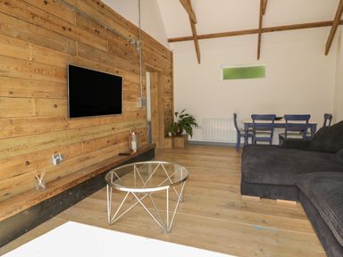 A living room with a mounted TV glass coffee table dark sofa dining table and chairs at The Corn Store in St Stephen