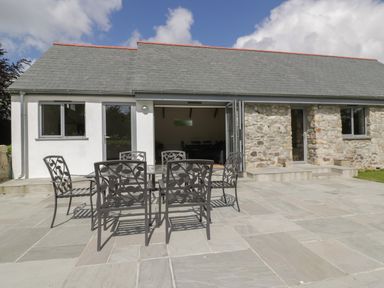 An outdoor patio with a glass table and six metal chairs in front of a building with stone and white walls at The Corn Store in St Stephen