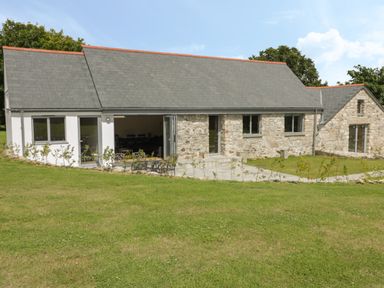 A stone and white exterior house with a large lawn and glass doors at The Corn Store in St Stephen