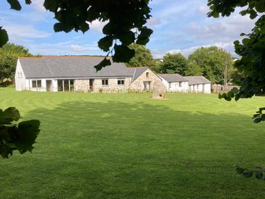A stone and white house with a grey roof set behind a large green lawn with trees around at The Corn Store in St Stephen