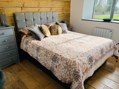 A bedroom with a bed with patterned bedding grey headboard side tables and a window at The Corn Store in St Stephen