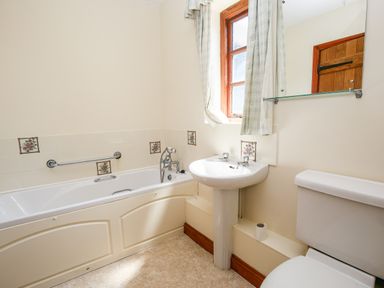 A bathroom with a bathtub a sink a toilet and a window with curtains at The Onibury in Craven Arms