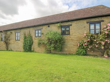 Exterior view of a stone building with black framed windows and climbing plants on a lawn at The Onibury in Craven Arms