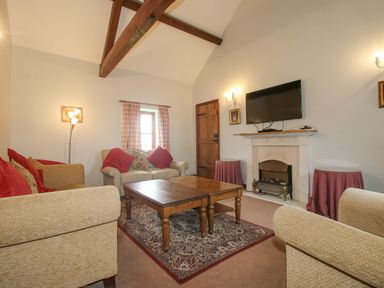 A living room with beige sofas red cushions wooden coffee table and a wall mounted tv at The Onibury in Craven Arms