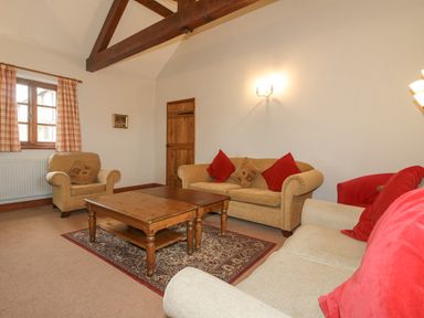 A living room with beige sofas red cushions a wooden coffee table and a window with checked curtains at The Onibury in Craven Arms