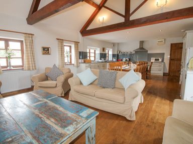 An open living room and kitchen with beige sofas wooden dining table and a blue rustic coffee table at The Onibury in Craven Arms