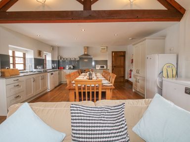 A kitchen with a long wooden dining table set with plates and chairs with a sofa in the foreground at The Onibury Craven Arms