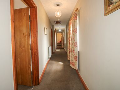 A hallway with carpeted floor wooden door and floral curtains on windows at The Onibury in Craven Arms