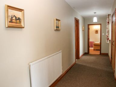A hallway with carpet flooring paintings on the walls a radiator and a view into a sitting room at The Onibury in Craven Arms