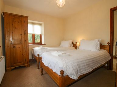 A bedroom with two single wooden beds a wooden wardrobe and a window at The Onibury in Craven Arms