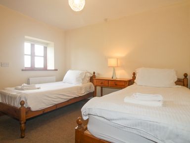 A bedroom with two single beds a wooden nightstand and a window at The Onibury in Craven Arms