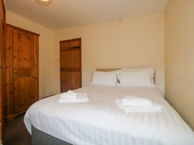 A bedroom with a double bed and white linens with towels and wooden wardrobe and door at The Onibury in Craven Arms