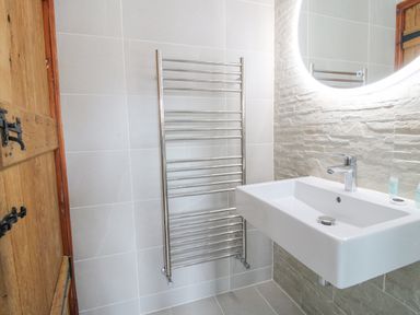 A bathroom with a wall-mounted sink a lit circular mirror a heated towel rail and a wooden door at The Onibury in Craven Arms
