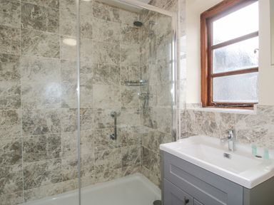 A bathroom with a tiled shower enclosure and a sink under a window at The Onibury in Craven Arms