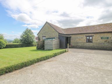 A stone building with a tiled roof next to a lawn and hedges at The Onibury in Craven Arms