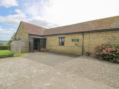 An exterior view of a stone building with a tiled roof and a parking area at The Onibury in Craven Arms