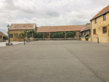 An outdoor tennis court surrounded by stone buildings with tiled roofs at The Onibury in Craven Arms