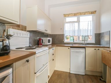 A kitchen with white cabinets a stove dishwasher and window with curtains at Stable Cottage in Triscombe