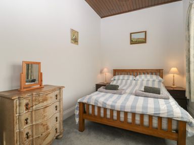 A bedroom with a wooden bed with striped bedding two bedside tables with lamps and a wooden dresser with a mirror at Stable Cottage in Triscombe