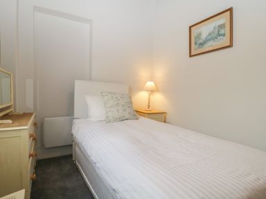 A bedroom with a single bed a bedside table with a lamp a chest of drawers and a framed picture on the wall at Stable Cottage in Triscombe