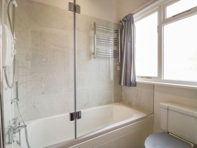 A bathroom with a bathtub shower combination towel rail and window at Stable Cottage in Triscombe