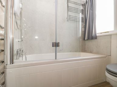 A bathroom with a bathtub shower combination and window at Stable Cottage in Triscombe