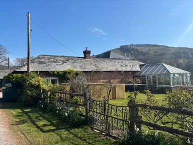 A cottage with a glass conservatory and garden behind a metal gate at Stable Cottage in Triscombe