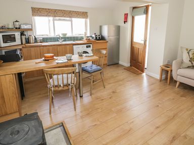 A kitchen and dining area with wooden cabinets chairs and table a refrigerator and a wooden door at The Wash House in Sibford Ferris