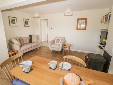 A dining table with cups and a cake in a living room with a sofa an armchair a television and a stove at The Wash House in Sibford Ferris