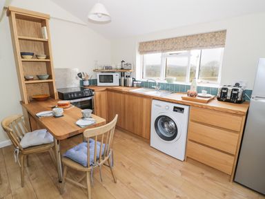 A kitchen with wooden cabinets a washing machine a microwave and a small dining area with chairs at The Wash House in Sibford Ferris