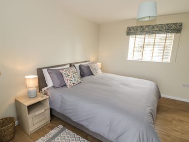 A bedroom with a double bed gray bedding and floral pillows bedside tables with lamps and a window with blinds and patterned valance at The Wash House in Sibford Ferris