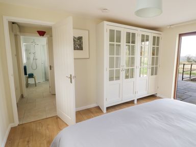 A bedroom with a white wardrobe an open door leading to a bathroom and a bed at The Wash House in Sibford Ferris