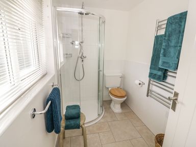 A bathroom with a shower enclosure toilet wooden stool and teal towels at The Wash House in Sibford Ferris