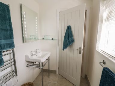 A bathroom with a white sink mirror glass shelf towels on a door and towel racks at The Wash House in Sibford Ferris