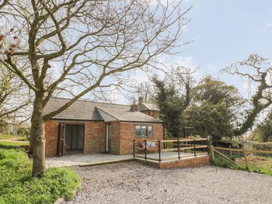 A brick house with a small patio and a bench surrounded by trees and grass at The Wash House in Sibford Ferris