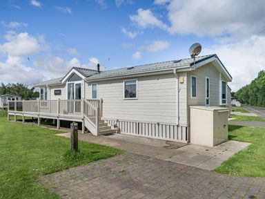 A white modular home with a porch and steps on a grassy plot at Links Lodge in Flookburgh