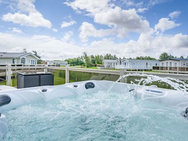 A hot tub with water jets on a deck overlooking mobile homes and grassy area at Links Lodge in Flookburgh