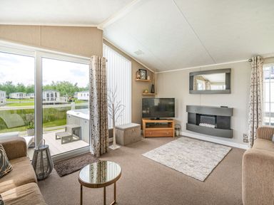 A living room with a television mirror and fireplace by sliding glass doors at Links Lodge in Flookburgh