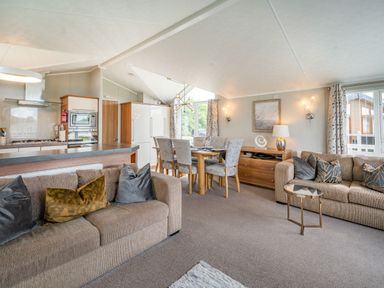 A living room and dining area with brown sofas a wooden dining table with chairs and a kitchen with appliances at Links Lodge in Flookburgh
