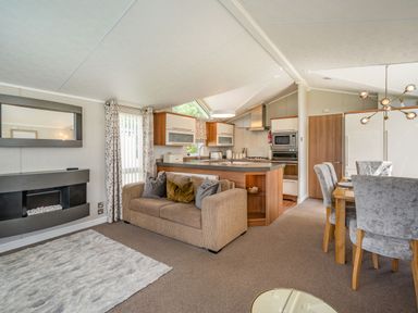 A living room with a sofa and a fireplace next to an open kitchen and dining area at Links Lodge in Flookburgh