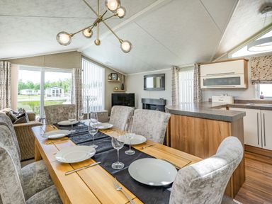 A dining area with a wooden table set with plates and glasses next to a living room and kitchen at Links Lodge in Flookburgh