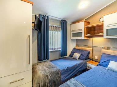 A bedroom with two single beds blue bedding bedside table and a wall-mounted tv at Links Lodge in Flookburgh