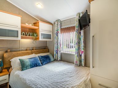 A bedroom with a bed a window with curtains and a wall-mounted TV at Links Lodge in Flookburgh