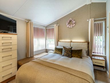 A bedroom with a bed pillows chest of drawers and windows with vertical blinds at Links Lodge in Flookburgh