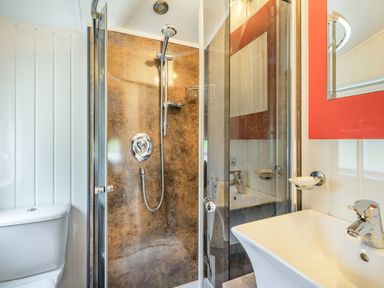 A bathroom with a toilet, glass shower enclosure, brown shower wall, white sink, and a mirror with a red frame at Links Lodge in Flookburgh