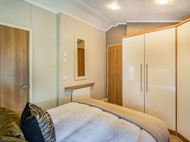 A bedroom with a bed a mirror on the wall and a wardrobe at Links Lodge in Flookburgh