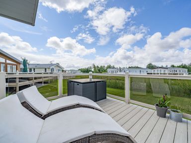 A deck with two lounge chairs small table and potted plants overlooking grassy area and nearby homes at Links Lodge in Flookburgh