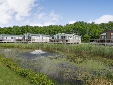 A small pond with green plants around and water fountain in front of white and wooden holiday lodges at Links Lodge in Flookburgh